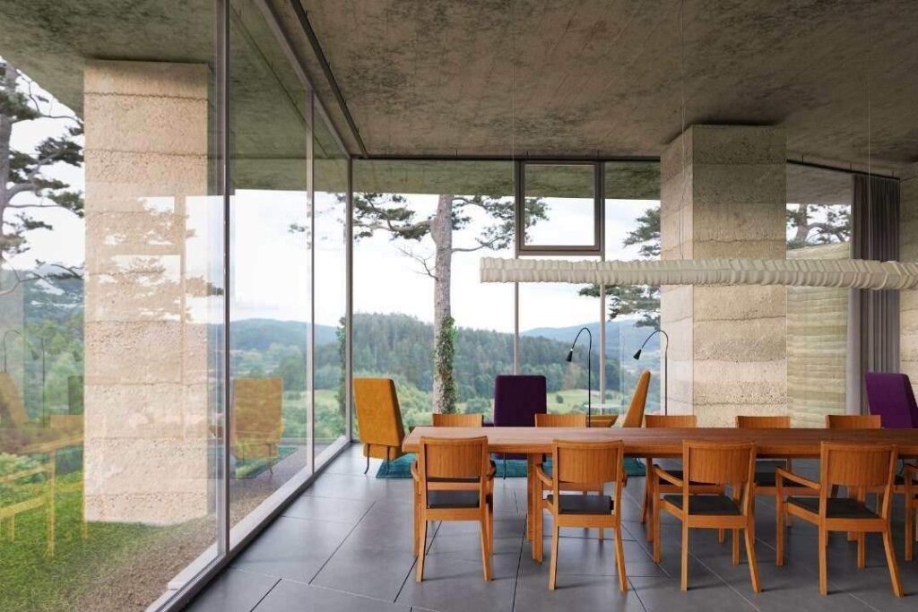 A 3D render showing a dining room with a long wooden table and large glass windows overlooking a forested landscape.