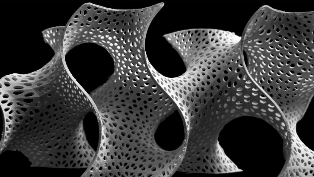 A close-up shot of a white, 3D-printed gyroid structure with intricate perforations set against a dark background.